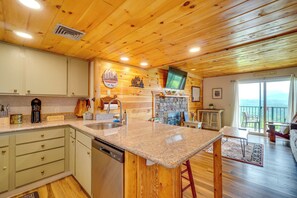 Eine Küche mit Granit-Arbeitsplatten, Holzschränken, einem Geschirrspüler und einem Kamin aus Naturstein.
