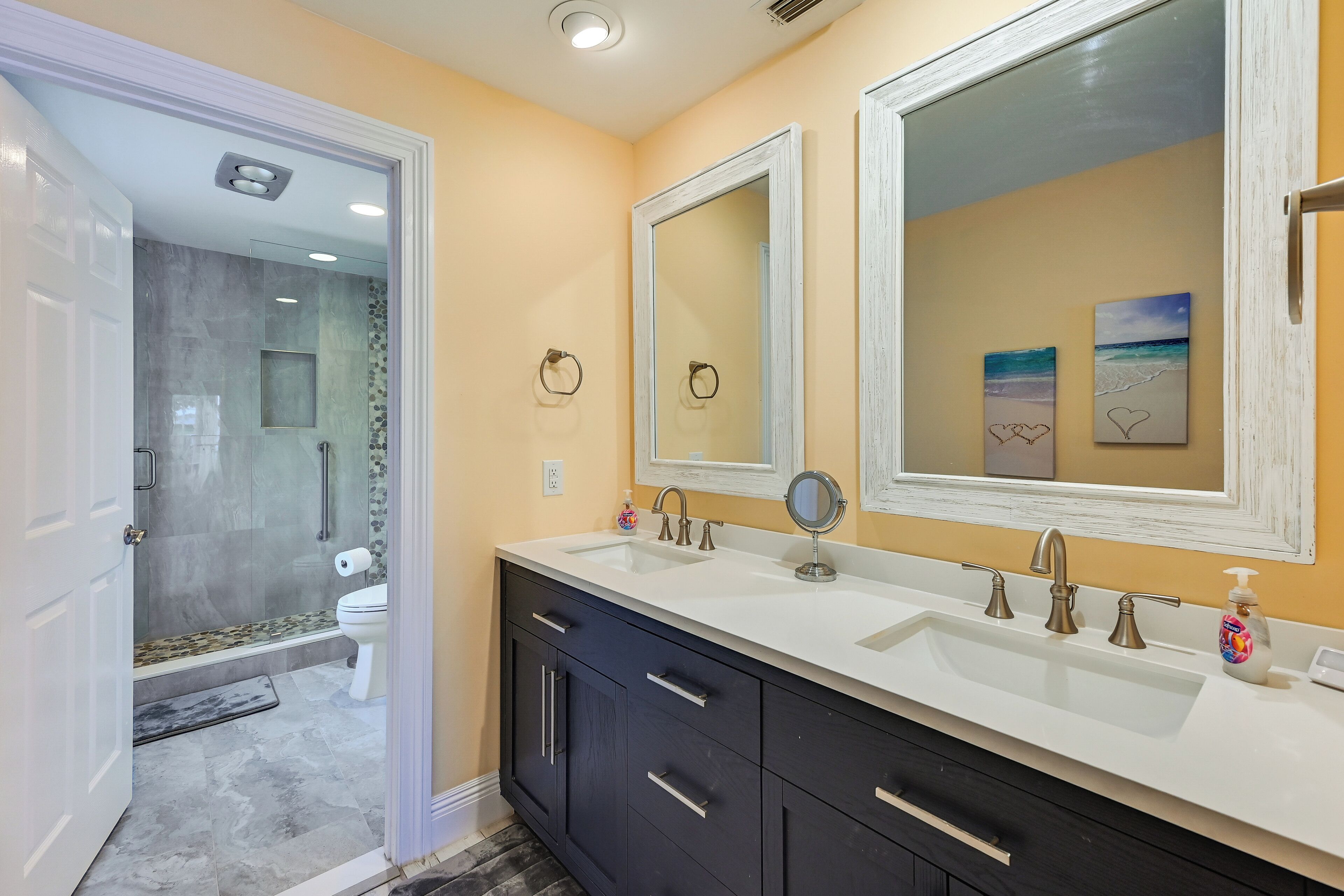 A bathroom with a double sink, two mirrors, a shower, and a toilet.