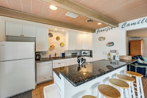 Een moderne keuken met witte kasten, een granieten eiland met barstoelen, en een magnetron.
