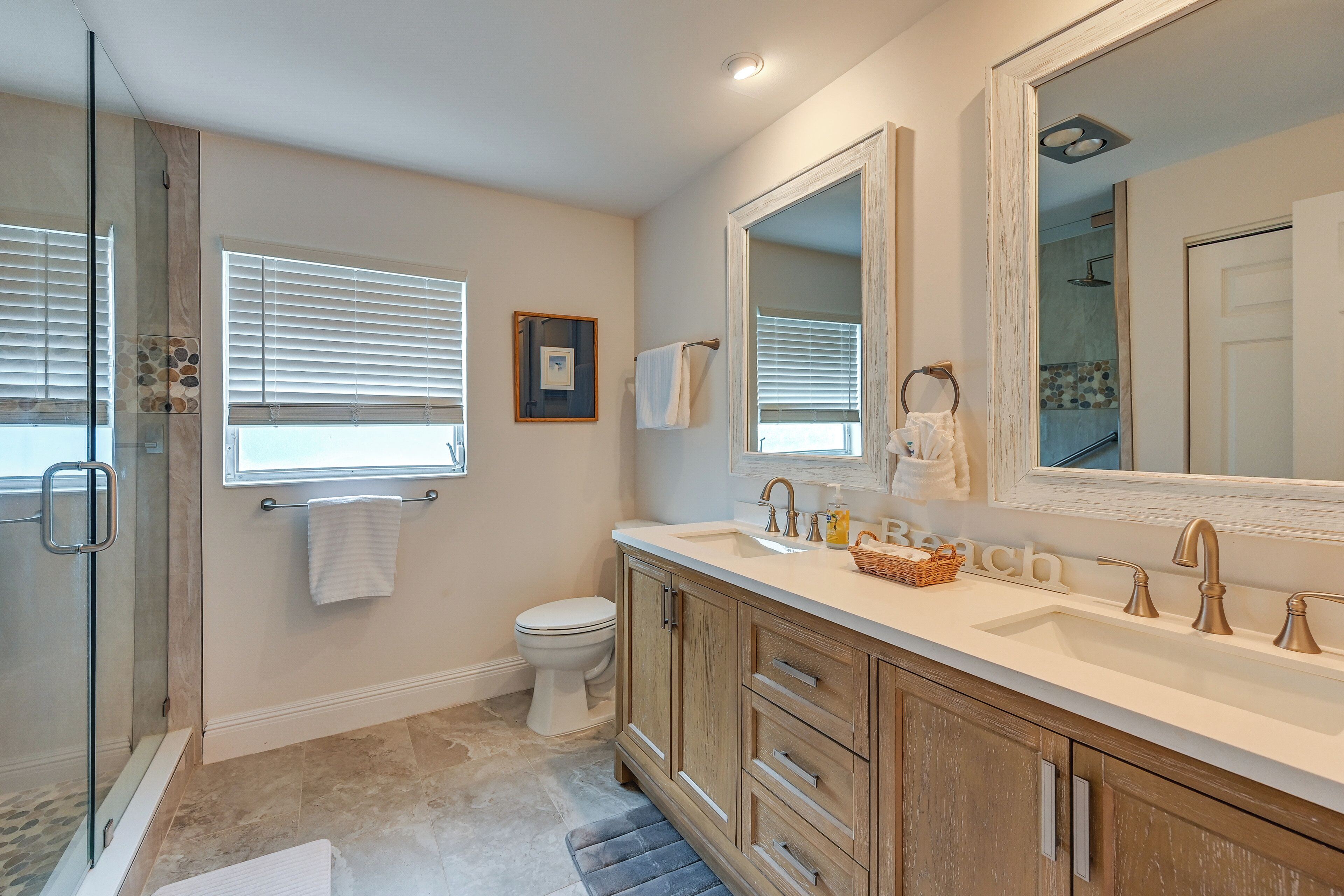 A bathroom with a glass shower enclosure, a toilet, a sink with a vanity, and a large mirror.