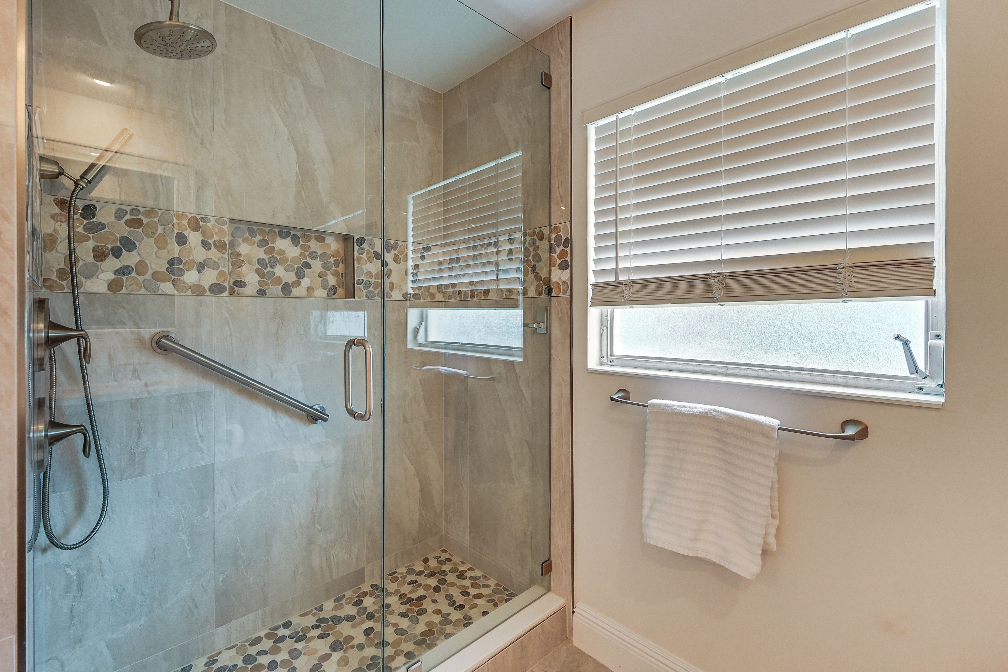 A shower with a glass door, a handrail, and a tiled floor.