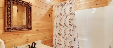 Un baño rústico con cabaña, con un espejo de marco de madera, un lavamanos con grifo, una cortina de ducha y un cabezal de ducha.