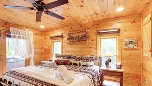 Une chambre dans une cabane en bois, avec un lit, une table de chevet et un ventilateur de plafond.