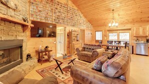 L’intérieur d’un chalet confortable, avec une cheminée, un mur en pierre, une bibliothèque, des meubles en cuir et un coin cuisine.