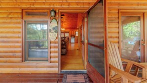 Une cabane en bois avec une pancarte accueillante, une véranda avec un fauteuil et une vue sur l’intérieur.