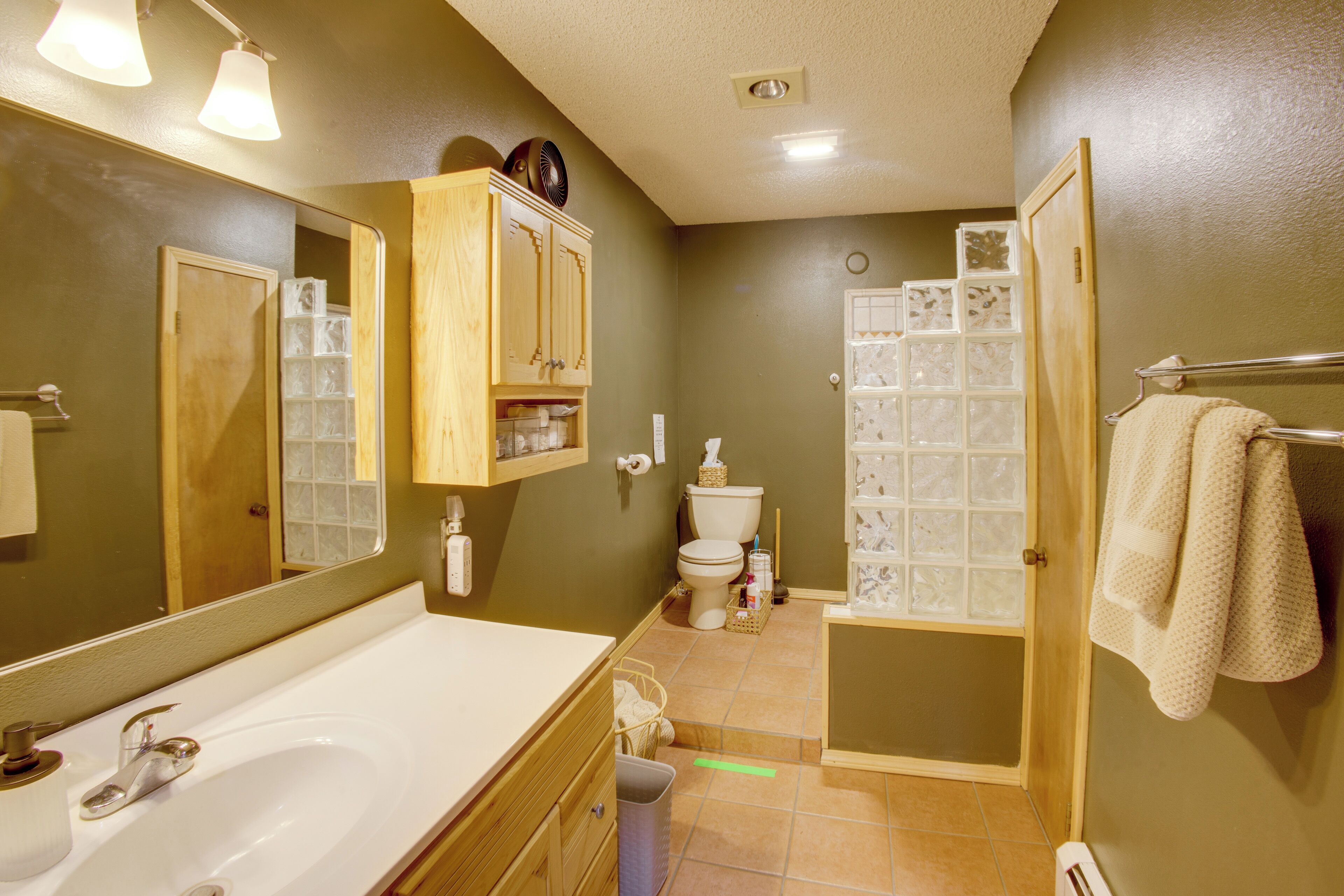 A bathroom with a large mirror, wooden cabinets, a bathtub, a toilet, and a shower area.