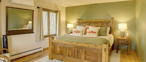 Un dormitorio con cama de madera, ventilador de techo, ventana con cortinas, espejo y mesita de noche con lámpara.