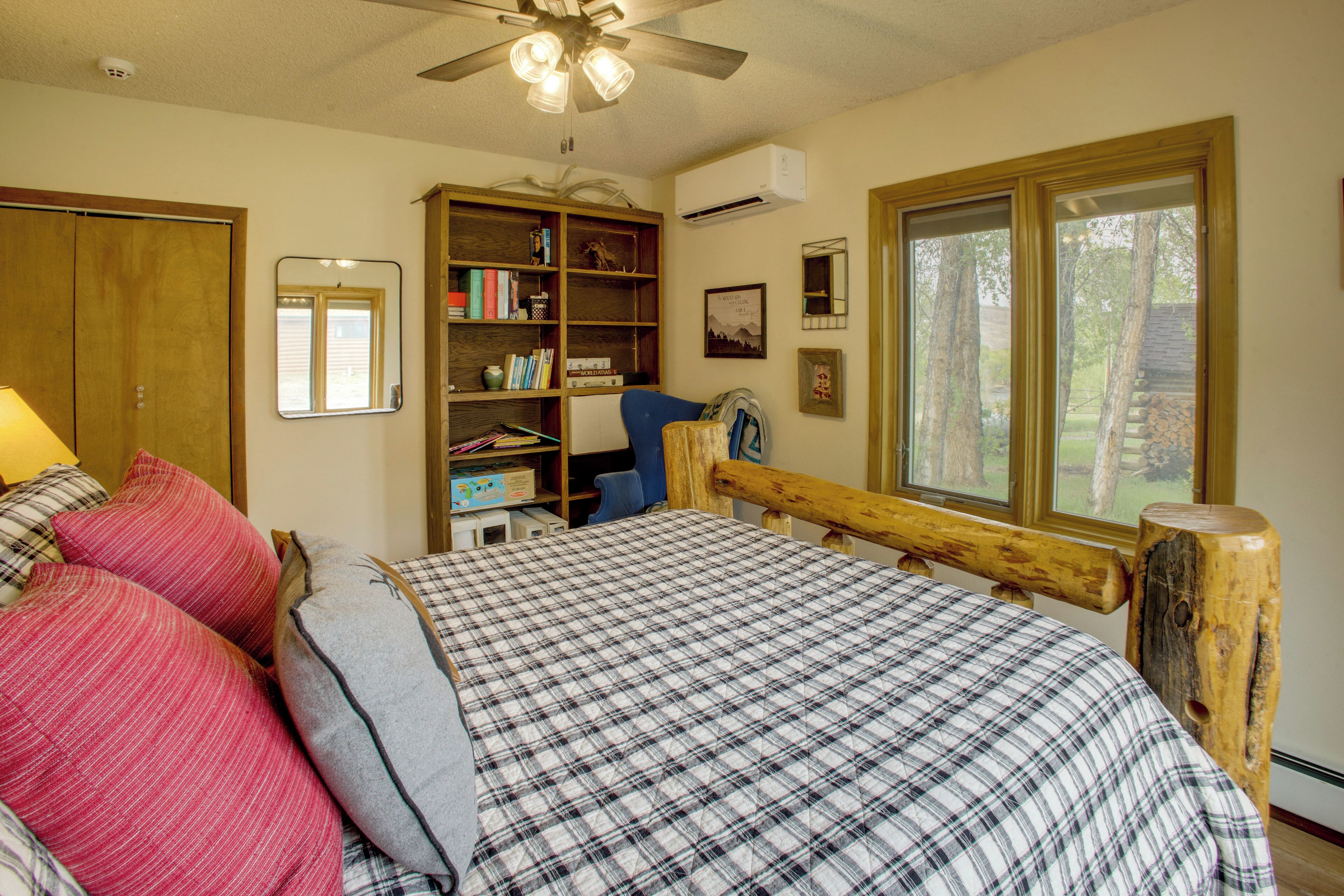 A bedroom with a bed, a wooden headboard, a bookshelf, a desk, and a window with a view of trees.