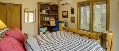 A bedroom with a bed, a wooden headboard, a bookshelf, a desk, and a window with a view of trees.