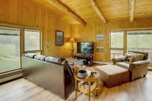 A wooden-paneled living room with a sofa, a chair, a television, and a fireplace. - Mtn-view Deck & Fire Pit! 2-cabin Retreat in Cody (Cody)