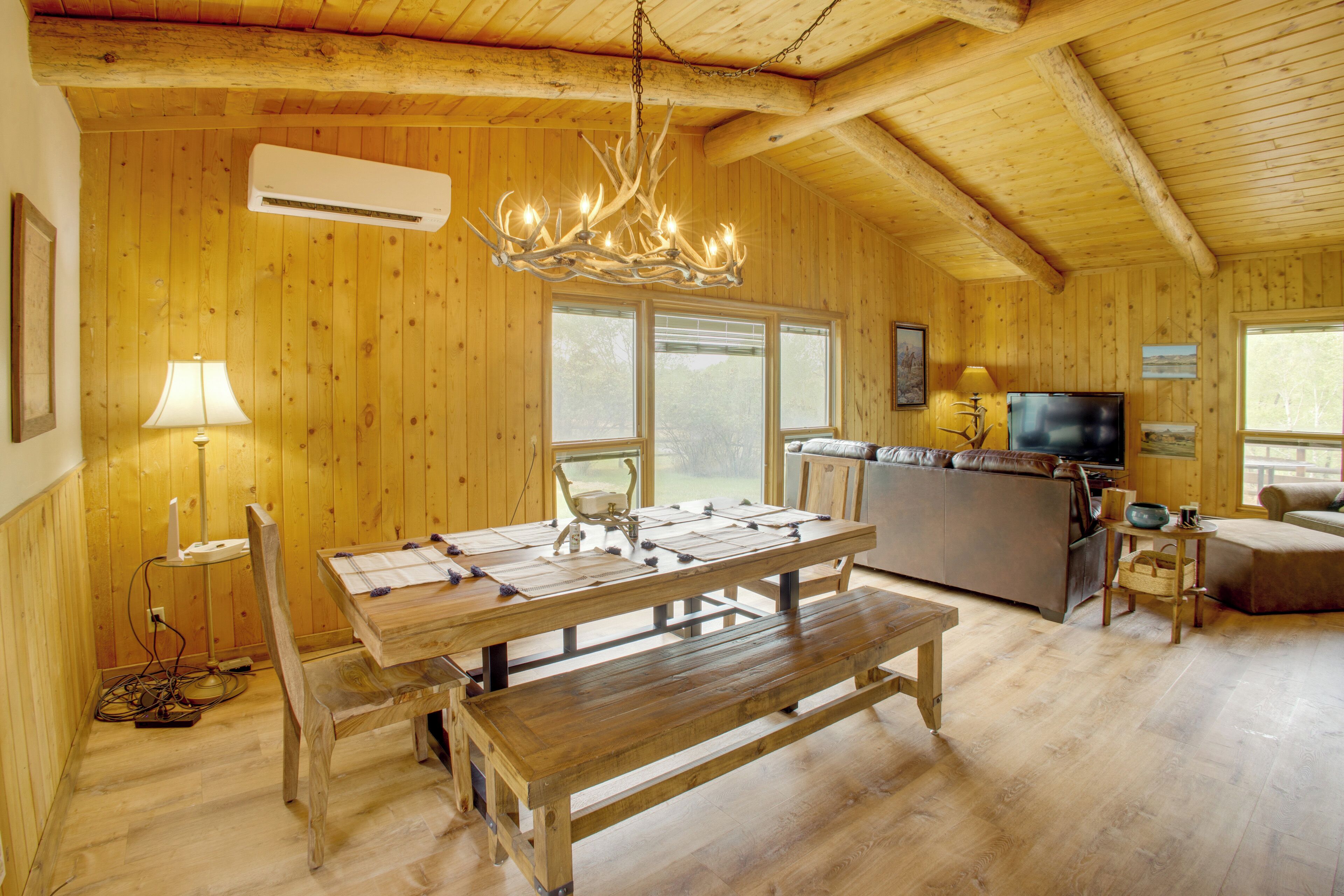 A wooden interior with a dining table, benches, a chandelier, a television, and a kitchen area.