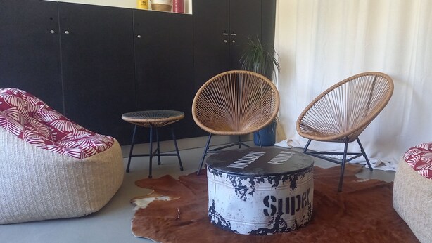 Una habitación con tres sillas de mimbre, una mesita redonda y un tapete de cuero de vaca.