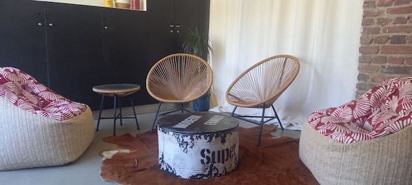 A room with three wicker chairs, a round drum table, and a cowhide rug.