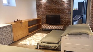 Una habitación pequeña y acogedora con pared de ladrillo, una cama, un televisor, un aparador de madera y una alfombra estampada.