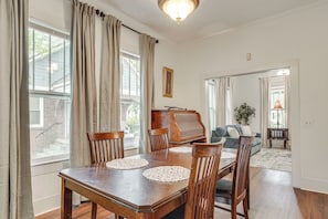 Een eetruimte met een houten tafel, stoelen, een piano en een bank op de achtergrond.