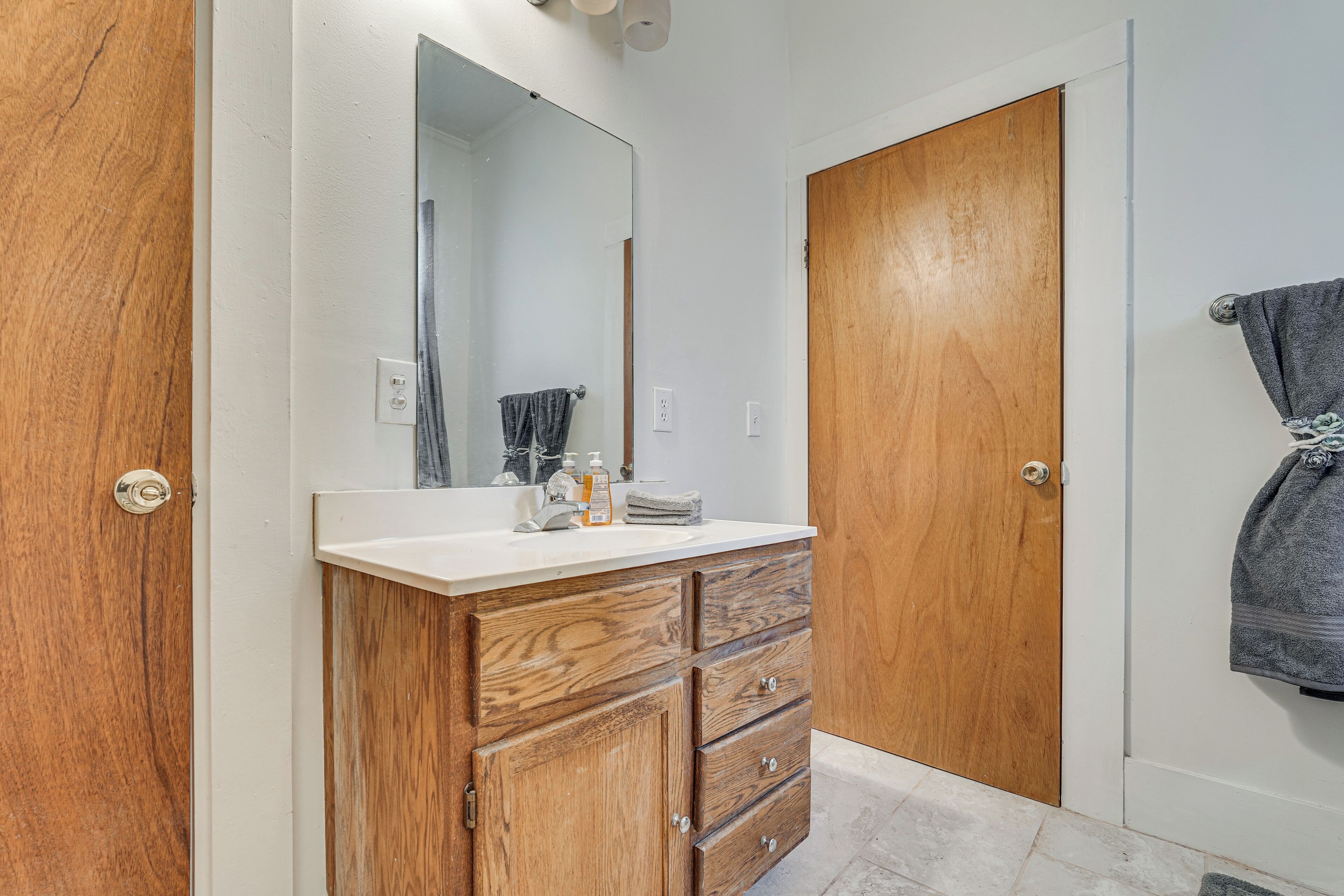 A bathroom with a wooden vanity, a mirror, a towel rack, and a door.