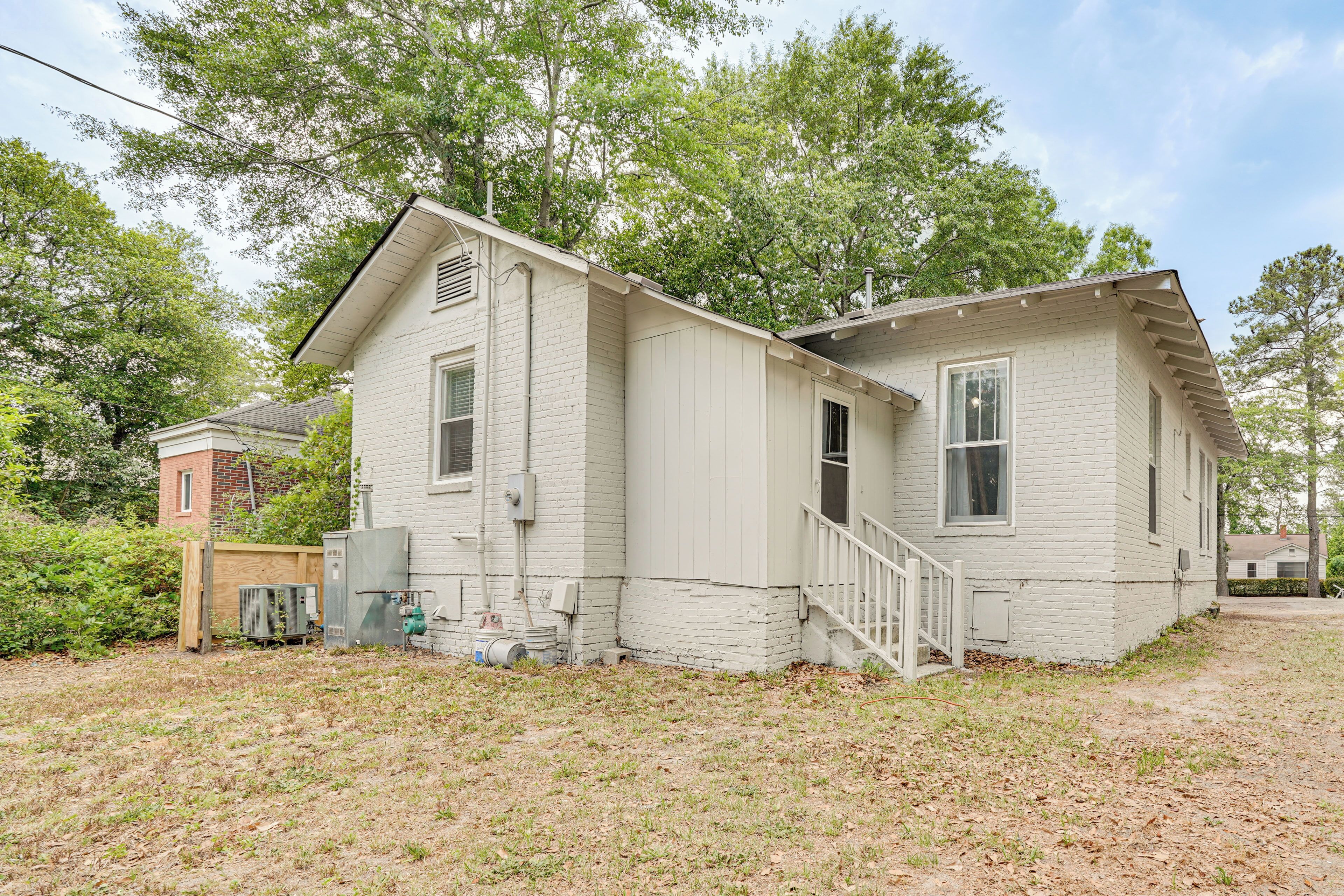 A single-story house with a front porch, a small attached garage, and a brick structure in the background.