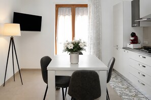 Una cuina moderna amb taula de menjador, cadires, televisor i una planta decorativa.