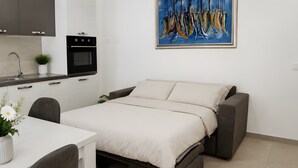 Una habitación compacta con una cama, una pequeña kitchenette, una mesa de comedor y un cuadro en la pared.