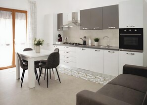 Una cuina moderna amb armaris blancs, una taula de dinar amb cadires, una placa de cocció i forn integrat.