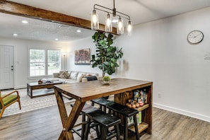 A dining area with a wooden table, bar stools, a hanging light fixture, a potted plant, and a clock on the wall. - < 2 Mi to Dallas Stadium! Work & Play Base w/ Yard (Arlington)