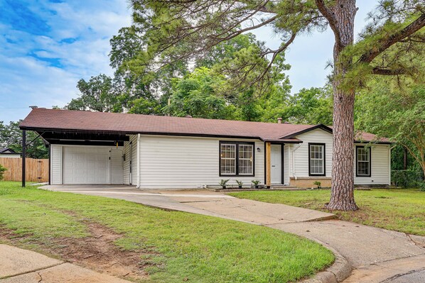 A single-story house with a garage, a covered porch, and a well-maintained lawn. - < 2 Mi to Dallas Stadium! Work & Play Base w/ Yard (Arlington)