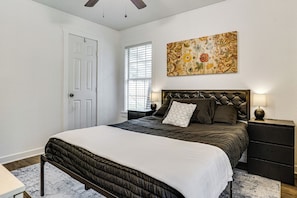 A bedroom with a bed, a nightstand, a wall-mounted lamp, a door, and a window with blinds. - < 2 Mi to Dallas Stadium! Work & Play Base w/ Yard (Arlington)
