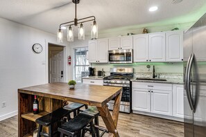A modern kitchen with white cabinets, stainless steel appliances, a wooden dining table, and pendant lighting. - < 2 Mi to Dallas Stadium! Work & Play Base w/ Yard (Arlington)