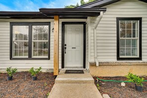 A house with a white exterior, a front door, two windows with black frames, and a small porch area with potted plants. - < 2 Mi to Dallas Stadium! Work & Play Base w/ Yard (Arlington)