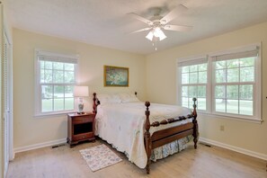 A bedroom with a wooden bed, two windows, a ceiling fan, and a nightstand with a lamp.