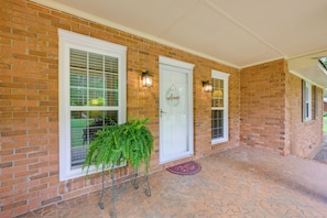 A brick house with a white door, two windows with shutters, and a potted plant.