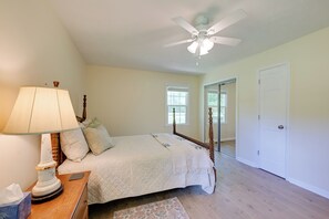 A bedroom with a bed, a nightstand, a lamp, a ceiling fan, and a door.