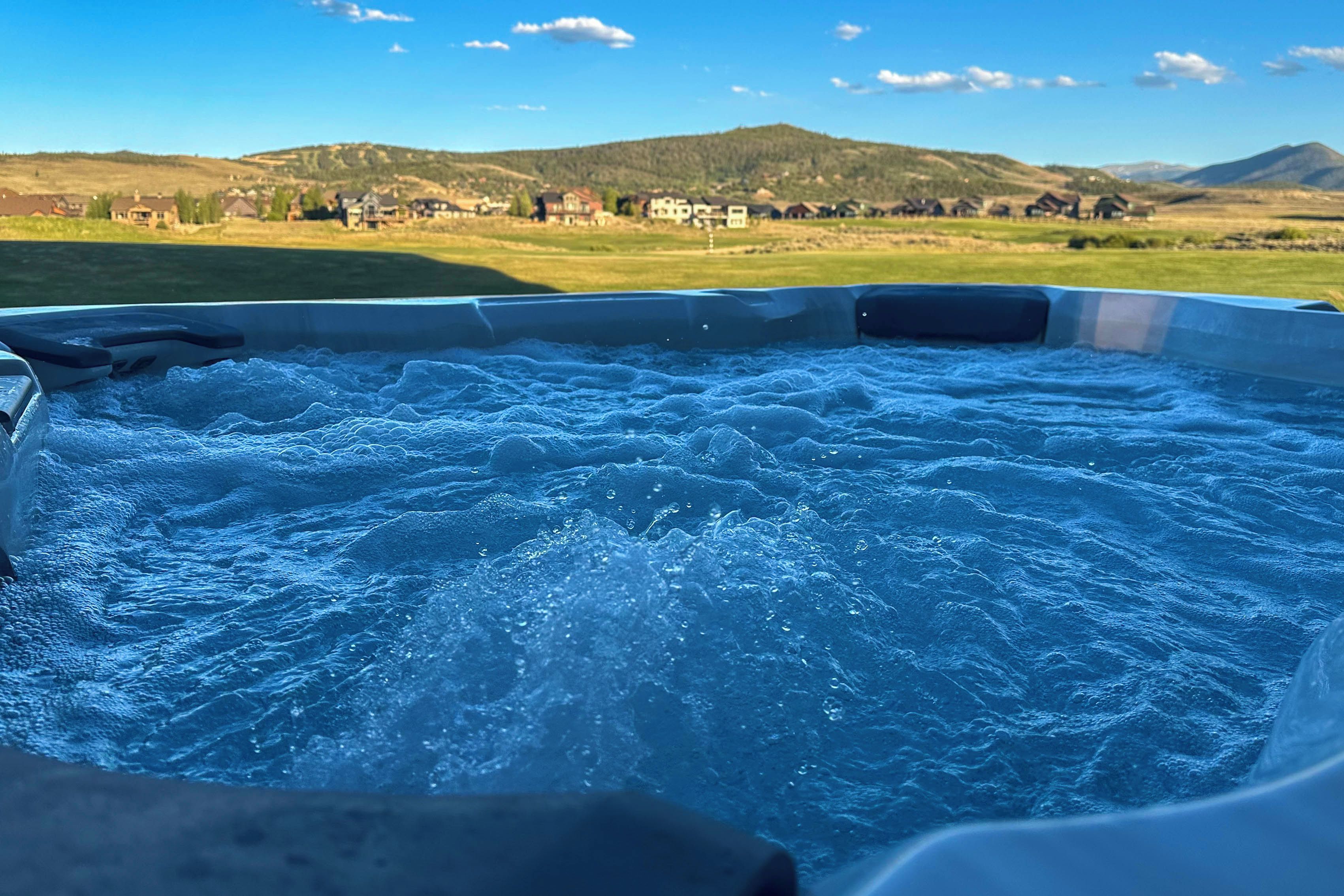 A hot tub with a view of a rural landscape and mountains in the background.
