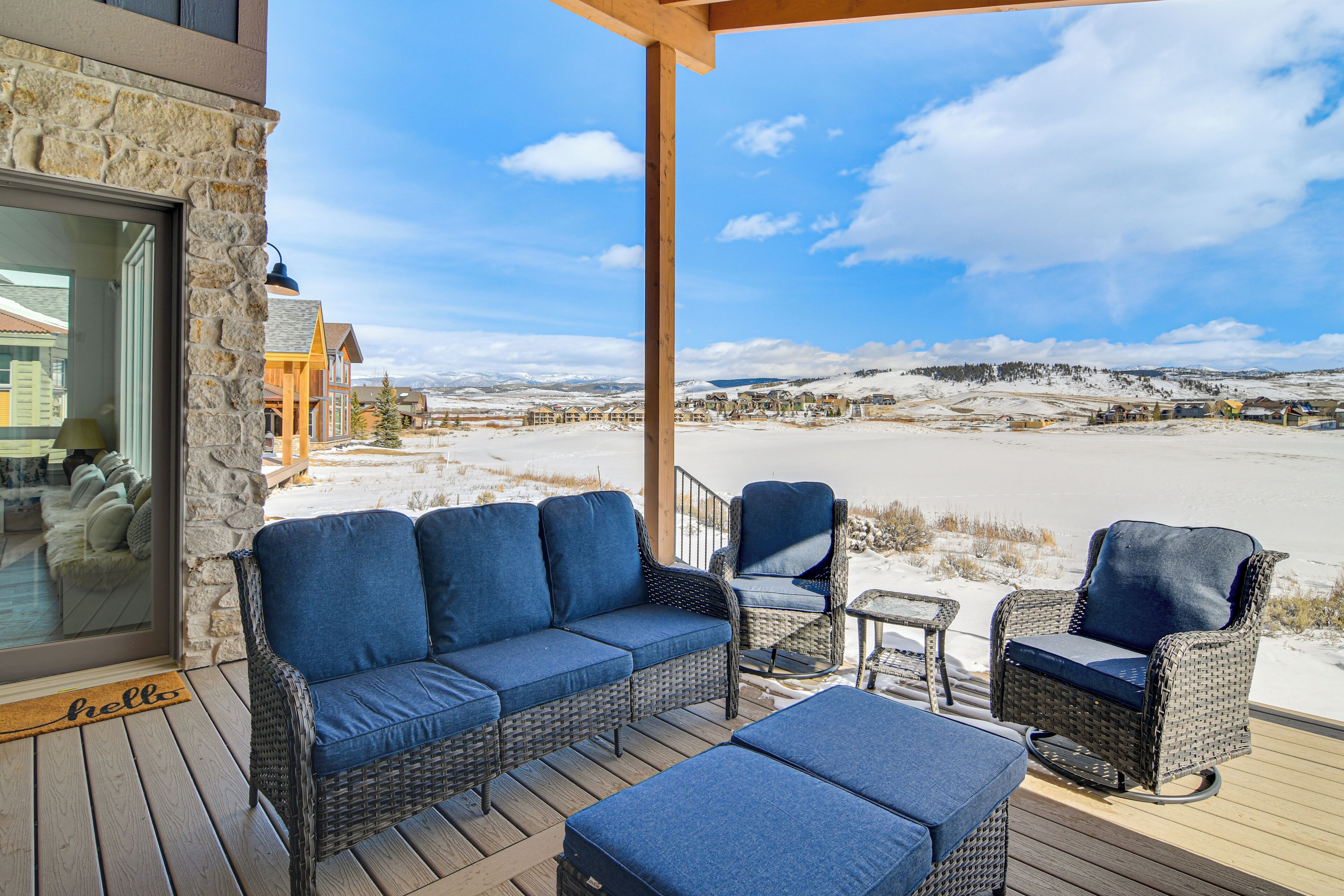 A covered outdoor seating area with wicker furniture, a stone wall, and a view of a snowy landscape.
