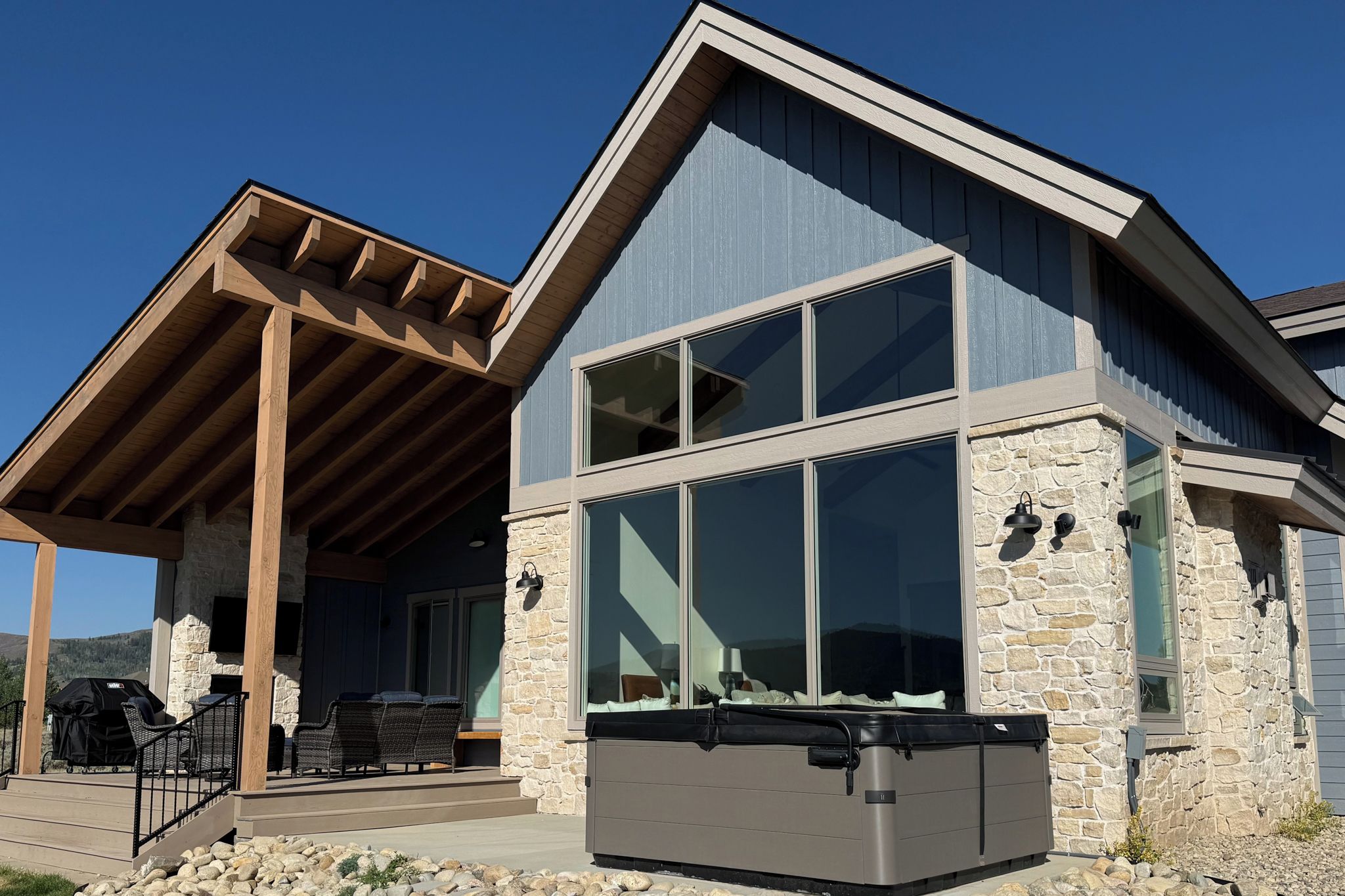 A modern house with a stone exterior, large windows, and a covered patio area.