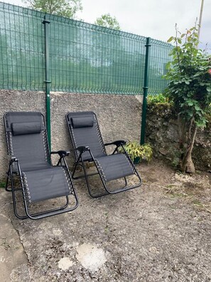 Dos sillones negros frente a una pared de piedra con una cerca verde al fondo.