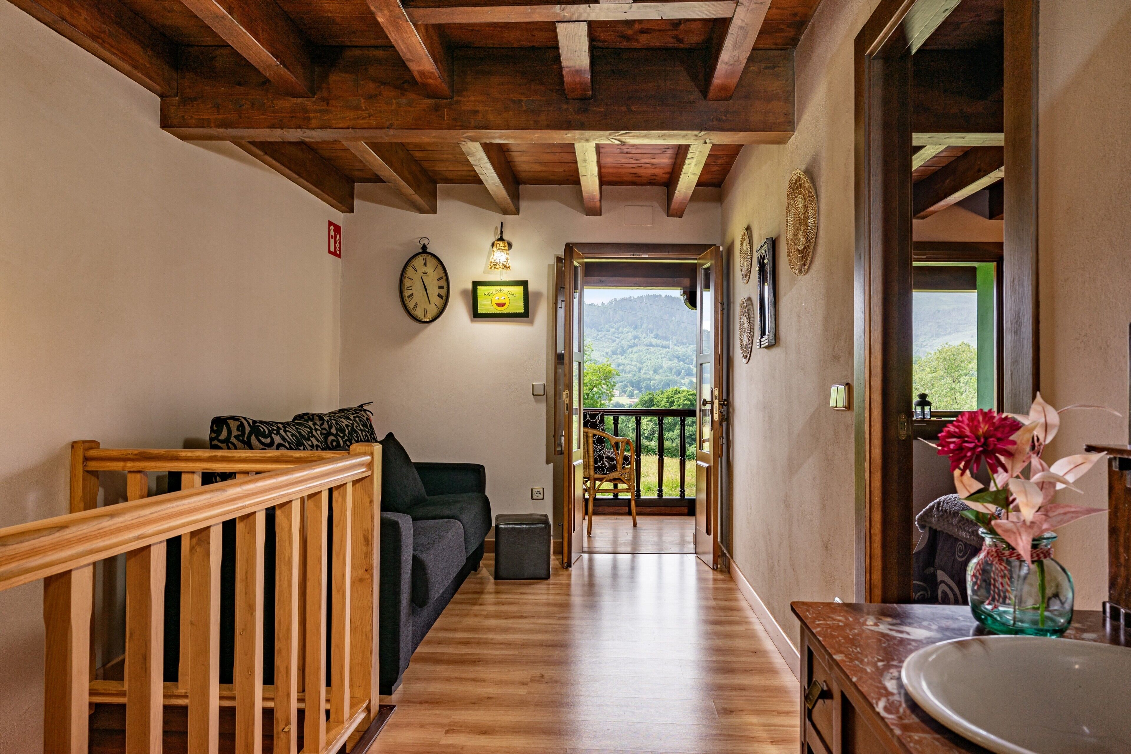 A wooden staircase leading to a balcony with a view of greenery. A sofa and a small table are visible in the room.