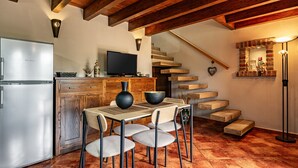 A kitchen with a refrigerator, wooden cabinets, a dining table with chairs, a television, and a staircase.