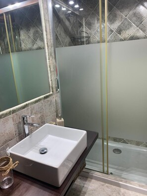 Un baño con un lavamanos blanco, un espejo y una cabina de ducha de vidrio.