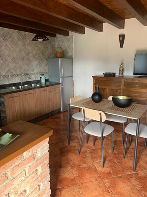 Una cocina con pared de ladrillo, un lavamanos, un refrigerador, una mesa de comedor con sillas y un televisor.