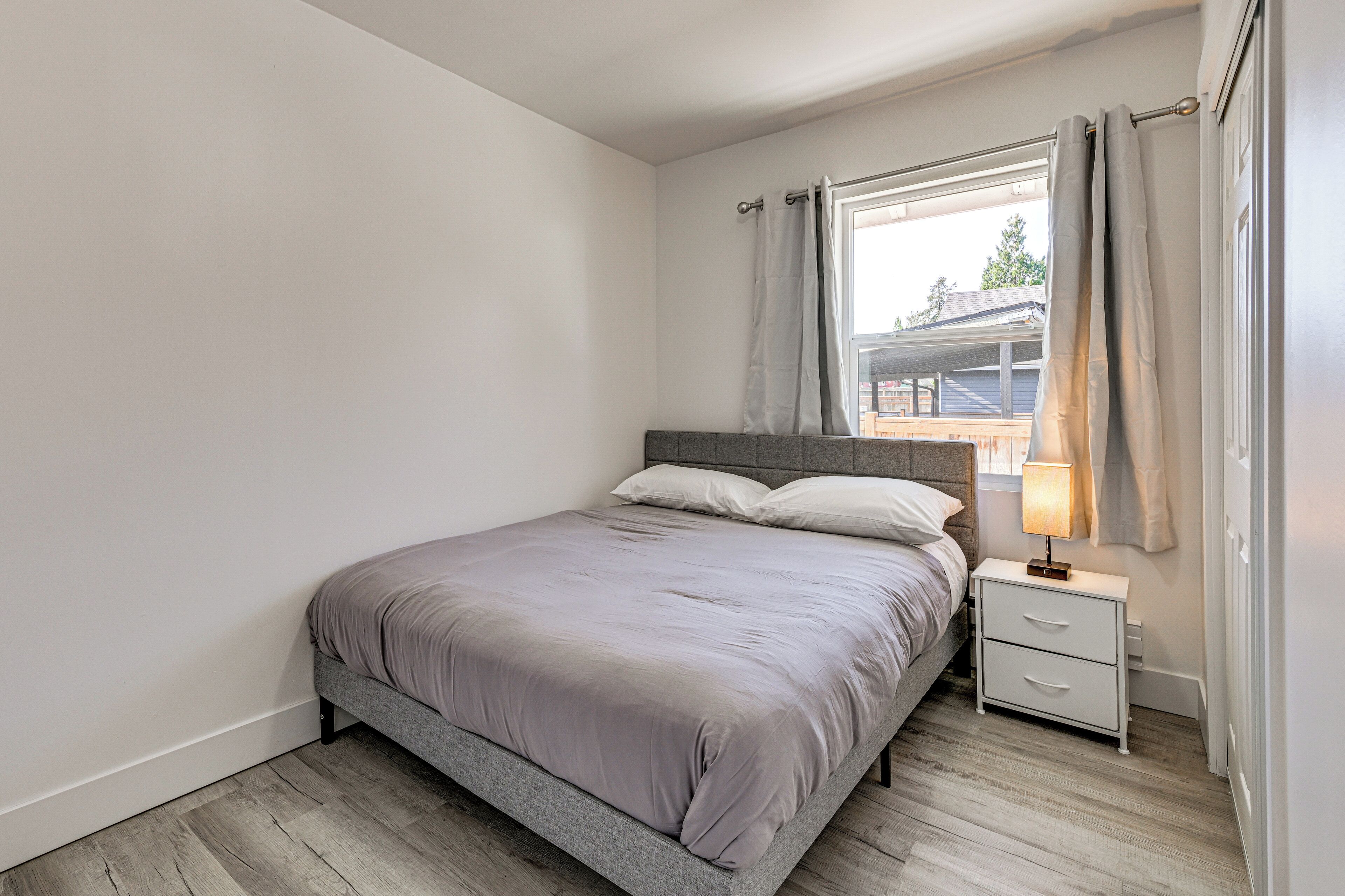 Een slaapkamer met een bed, nachtkastje en raam met gordijnen.