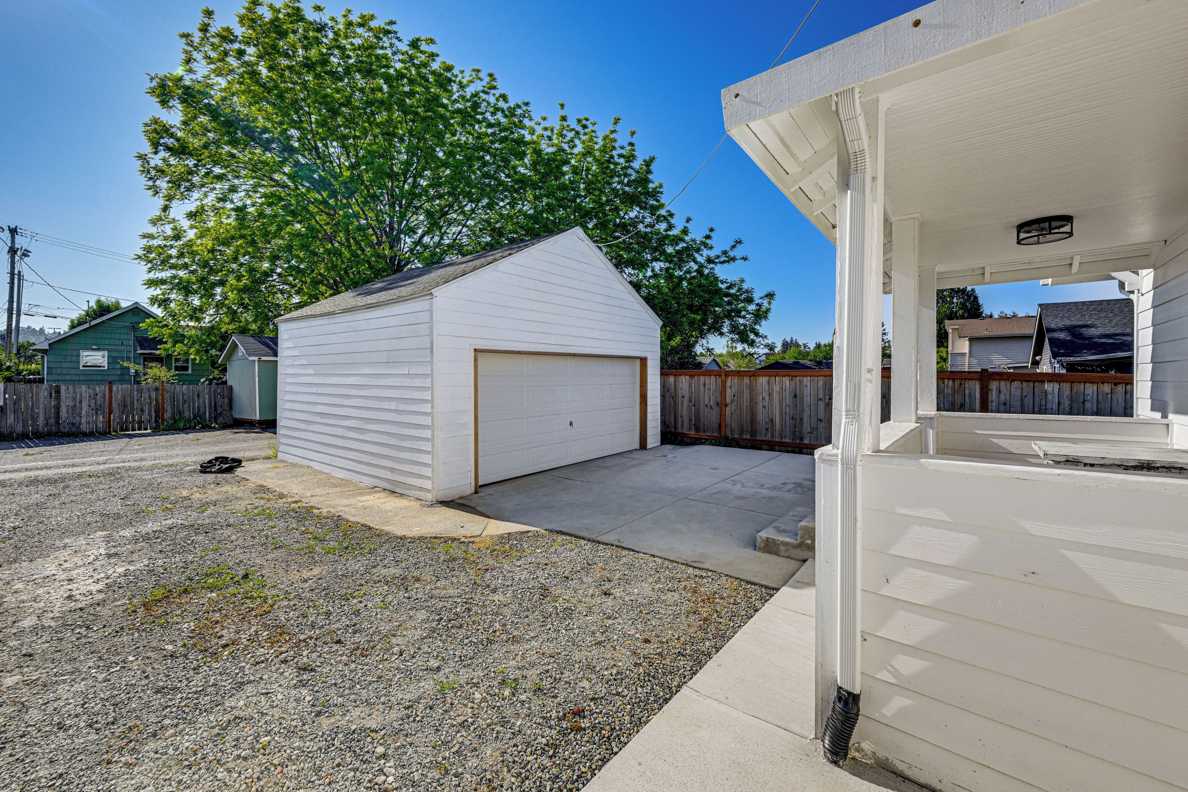 Un garage attenant à une maison, avec une allée en gravier et une clôture en bois.