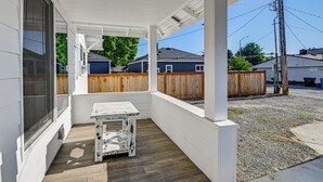 A covered porch with a table, wooden fence, and houses in the background. - Updated + Modern Craftsman Bungalow in Renton! (Renton)