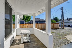 A covered porch with a table, wooden fence, and houses in the background.