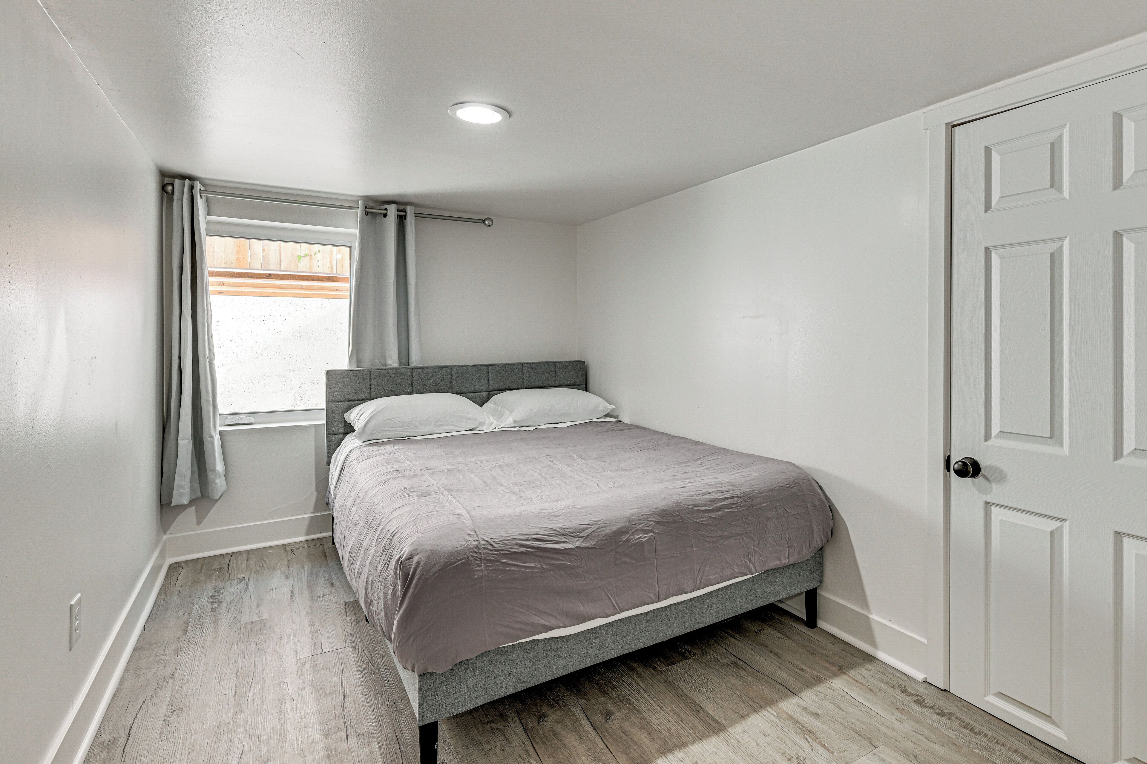 Een slaapkamer met een bed, een raam met gordijnen, een deur en een plafondlamp.
