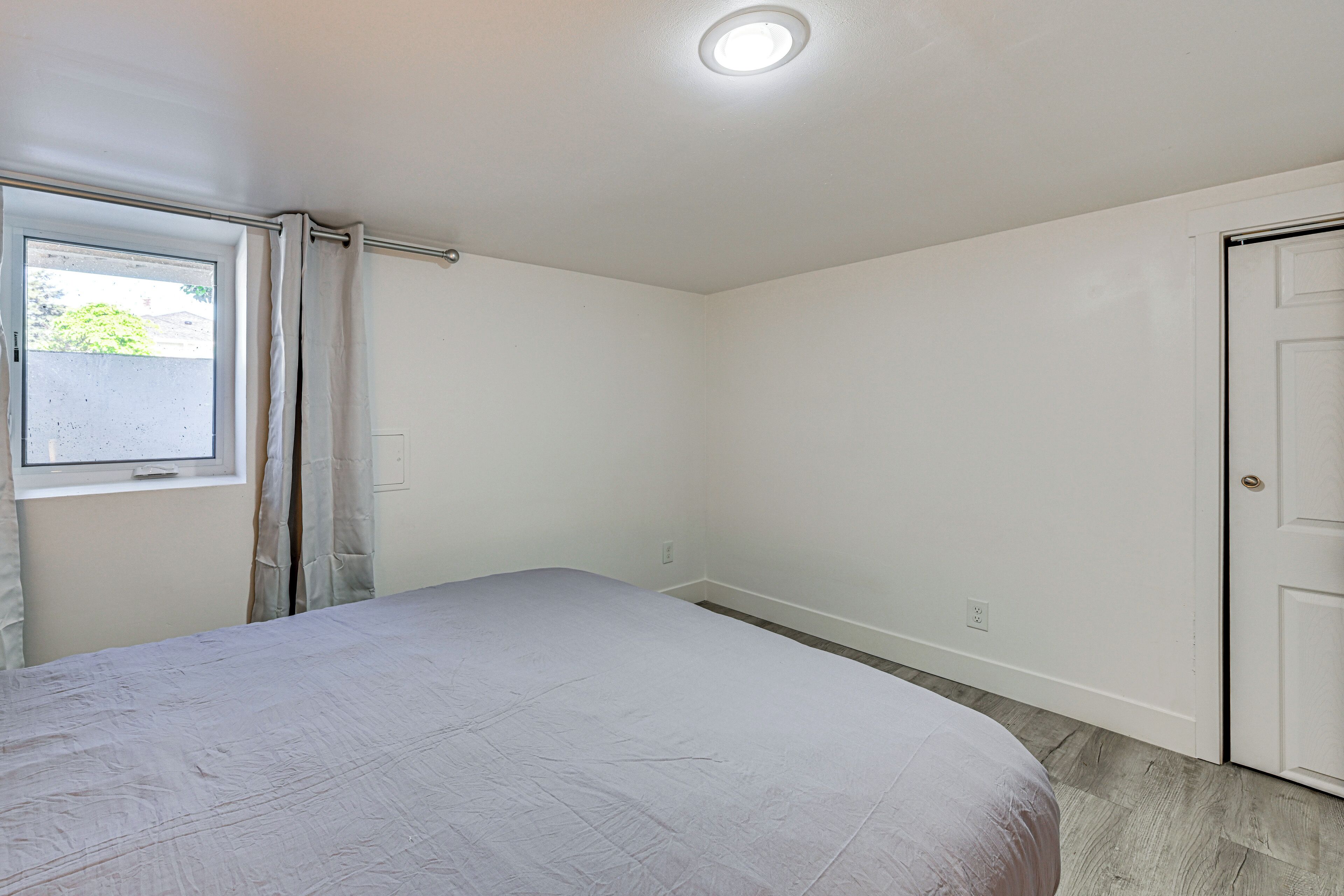 Une chambre à coucher avec un lit, une fenêtre avec des rideaux, une porte et un luminaire au plafond.