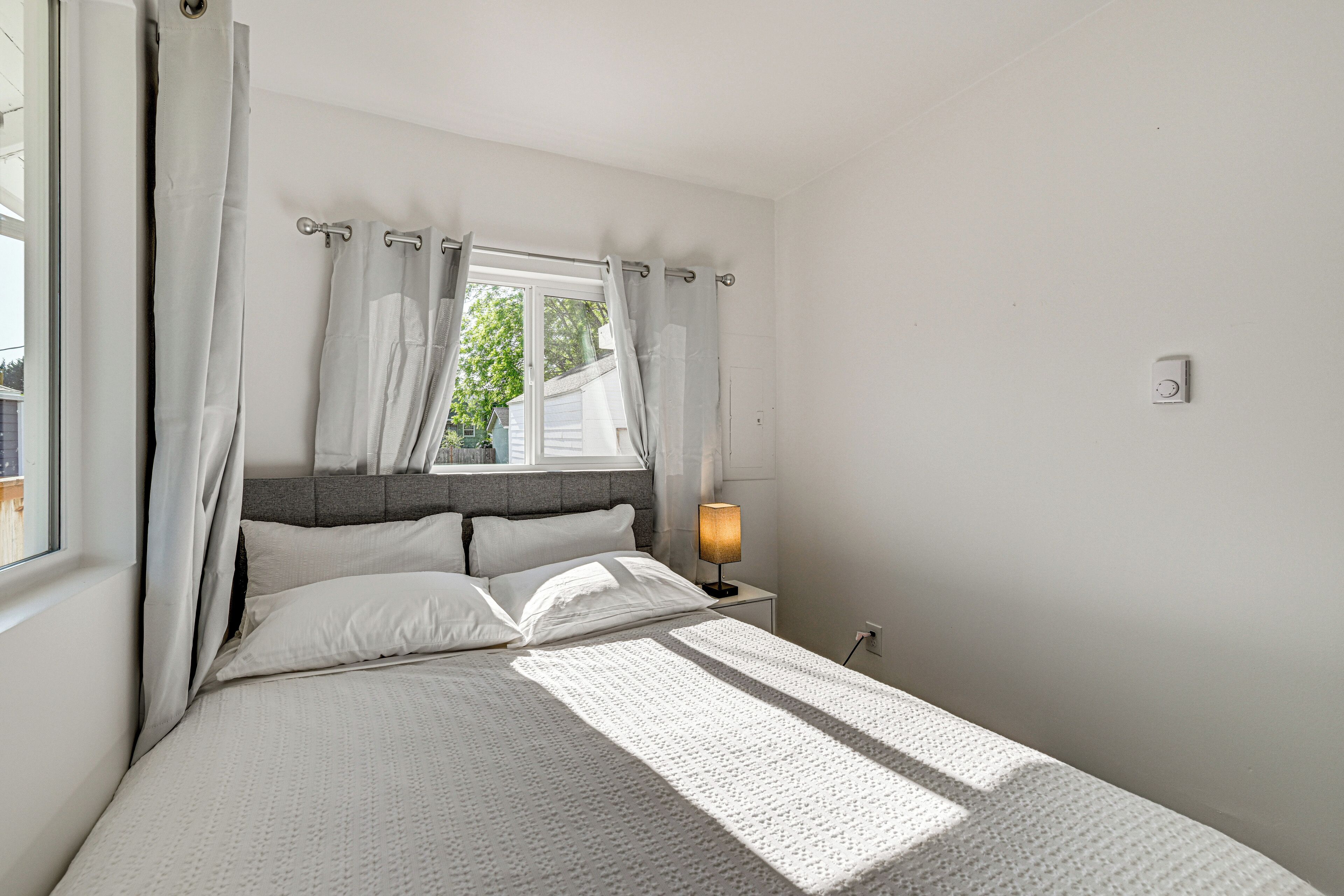 A bedroom with a bed, curtains, a nightstand, and a lamp.