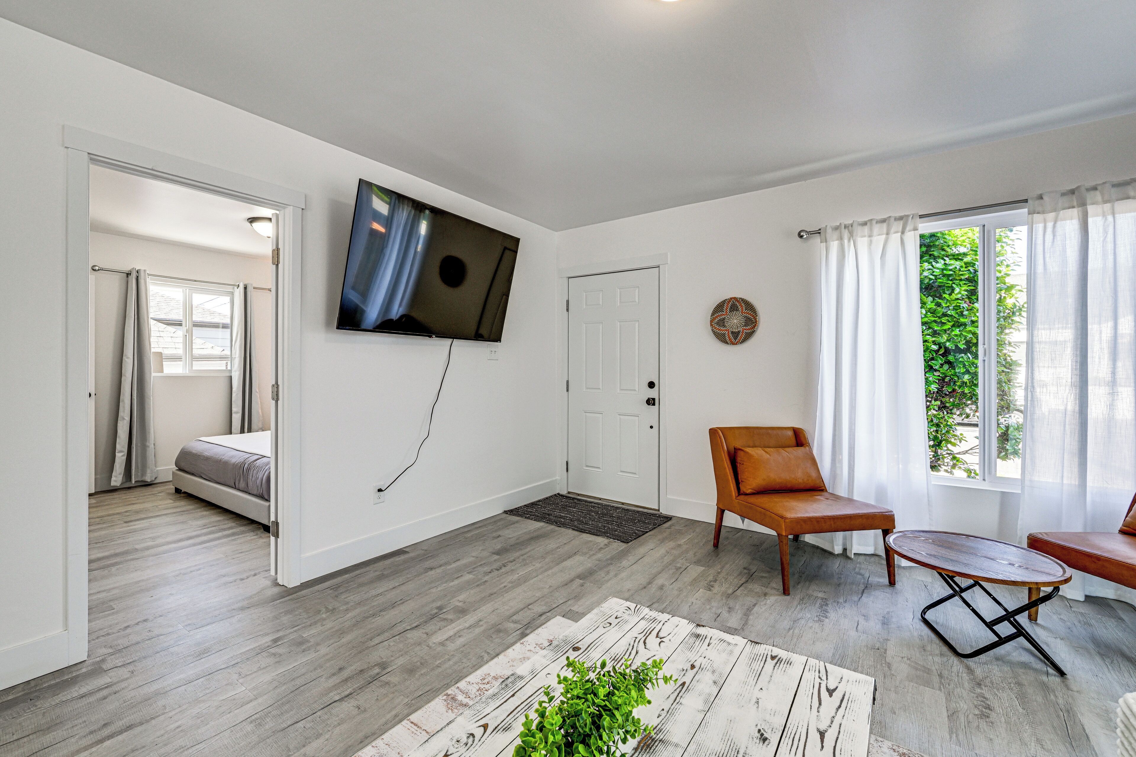 Uma sala de estar moderna com uma TV de tela plana, um sofá, uma mesa de centro e vista para um jardim pela janela.