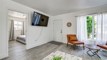 Uma sala de estar moderna com uma TV de tela plana, um sofá, uma mesa de centro e vista para um jardim pela janela.