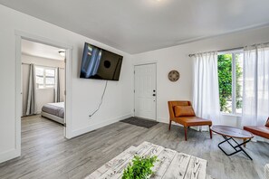 A modern living room with a flat-screen TV, a sofa, a coffee table, and a view of a garden through a window.